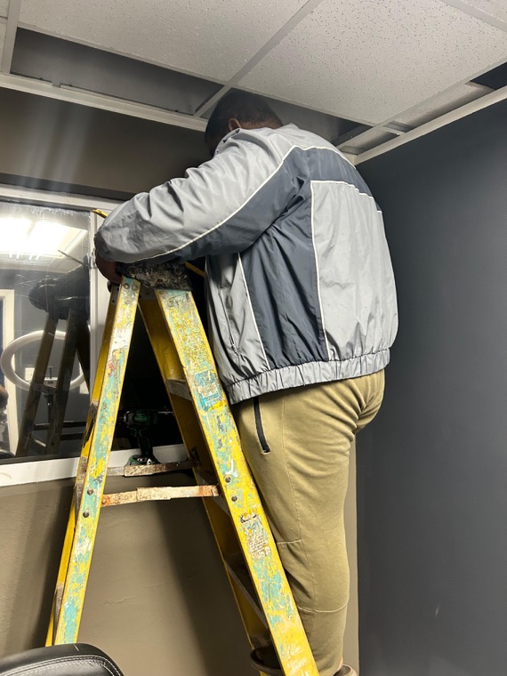 Ken up a ladder, rigging the room.